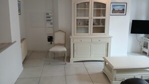 A room with a white cabinet, a chair, a television, and a tiled floor.