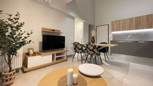 Een moderne woonkamer met een flatscreen televisie, een eethoek met stoelen, een ronde tafel en een potplant.