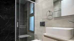 Een moderne badkamer met een douchecabine van glas, een wit toilet, een groot wastafelmeubel en een spiegel boven de wastafel.