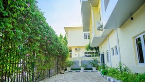 A courtyard with a paved walkway, a metal fence, and a building with multiple windows and balconies. - Bengerald Hotel And Suites (Abuja)