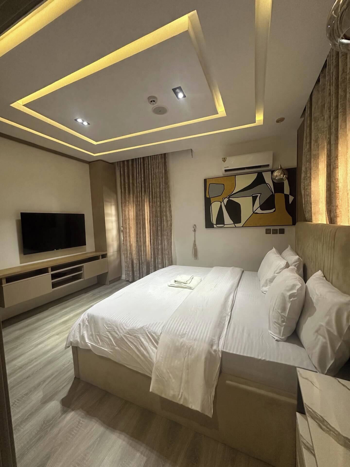 Una habitación de hotel moderna con una cama grande, un televisor de pantalla plana e iluminación empotrada en el techo.