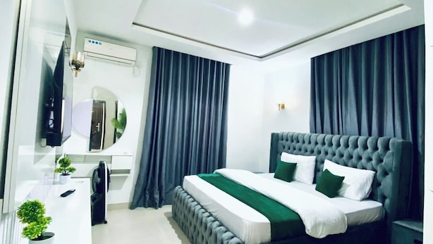 A modern bedroom with a tufted headboard bed, a white desk with a mirror, and a potted plant. - Bengerald Hotel And Suites (Abuja)
