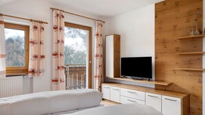 A bedroom with a bed, a TV, a wooden cabinet, and a window with curtains. - Apartment 'Mair Am Tinkhof Bergwohnung' with Mountain View, Shared Terrace and Wi-Fi (Selva dei Molini)