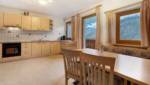 A kitchen with wooden cabinets, a dining table, chairs, a window with curtains, and a view of a snowy mountain. - Apartment 'Mair Am Tinkhof Bergwohnung' with Mountain View, Shared Terrace and Wi-Fi (Selva dei Molini)