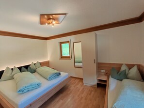 Ein Schlafzimmer mit hölzernem Kopfteil, einem Bett mit Kissen, einem Nachttisch, einem kleinen Fenster und einem Spiegel.