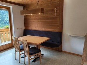 Ein Holztisch mit Stühlen, eine Bank und eine Holzwand mit einem Kreuz.