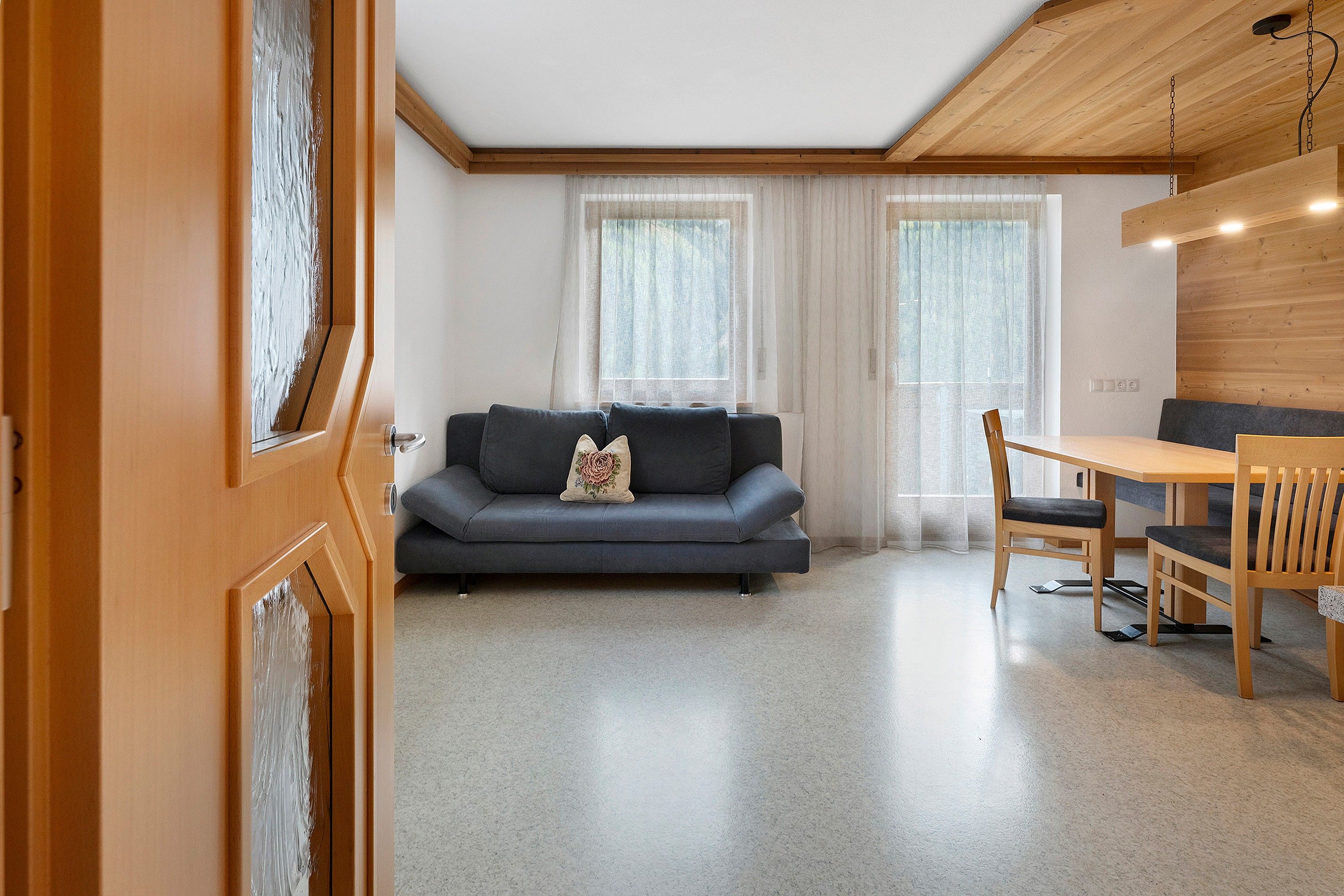 En moderne stue med sofa, spisebord med stole og træloft.