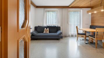 A modern living room with a sofa, a dining table with chairs, and a wooden ceiling.