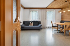 A modern living room with a sofa, a dining table with chairs, and a wooden ceiling.