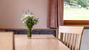 Une table à manger ornée d’un vase de fleurs, une chaise, et une vue sur la verdure à l’extérieur.
