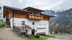 Un chalet de montagne doté d’un balcon en bois, d’un escalier en pierre et offrant une vue sur des montagnes enneigées.