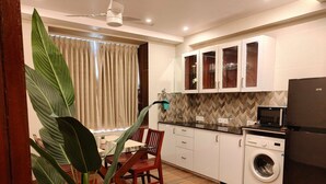 A compact kitchen with a washing machine, a microwave, and cabinets. - Townhouse Aiims Kolkata Tanishq Inn (Kalyani)