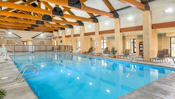 An indoor swimming pool with wooden beams, lounge chairs, and a tiled floor. - 3BR in resort near West Entrance, Pool, Hot Tub. (West Yellowstone)