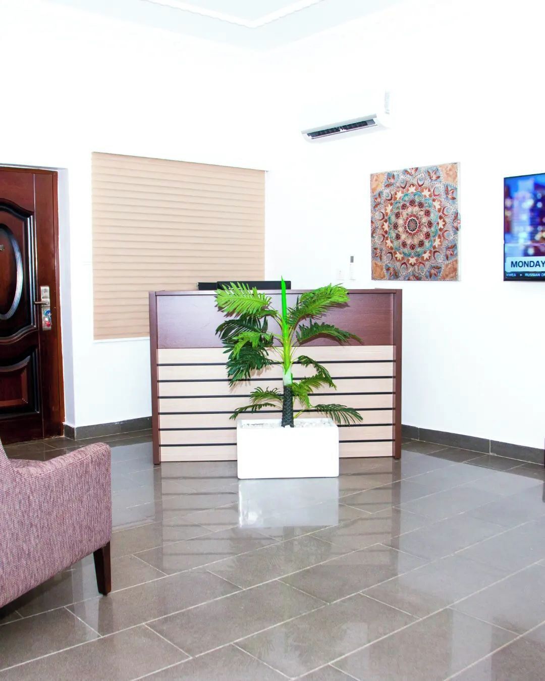 A reception area with a wooden desk, a potted plant, a pink chair, and a wall-mounted air conditioner.
