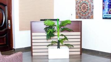 A reception area with a wooden desk, a potted plant, a pink chair, and a wall-mounted air conditioner.