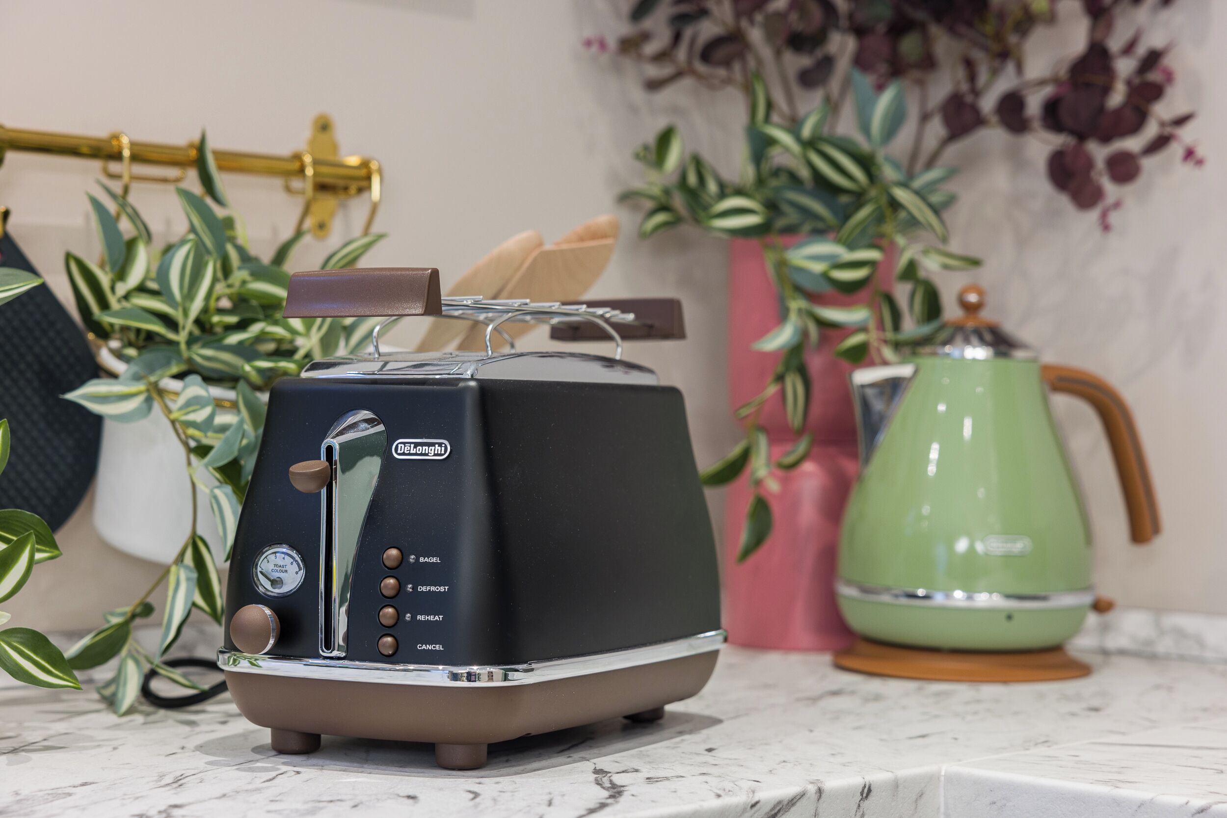 Cozinha com torradeira preta, chaleira verde e plantas em vasos.