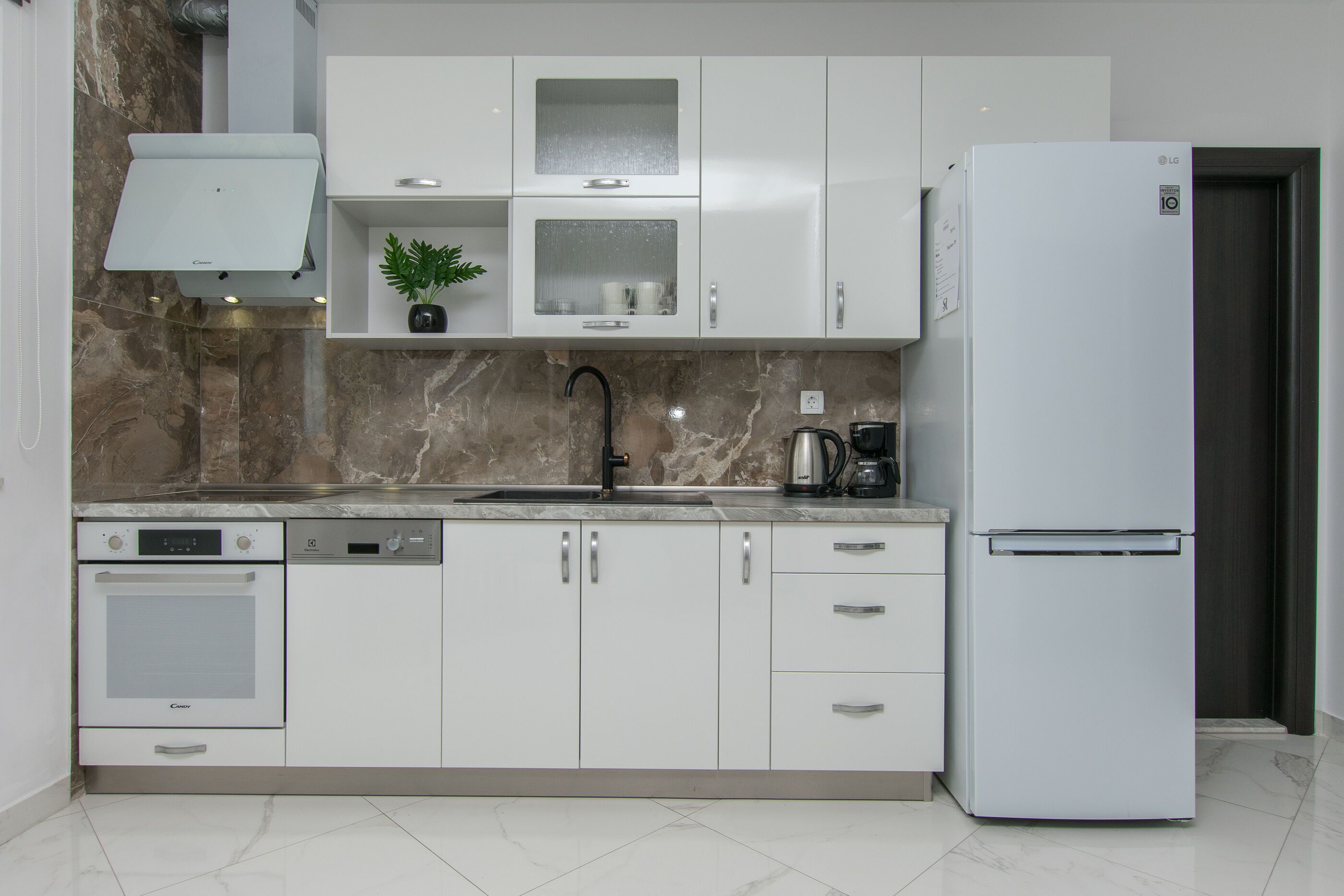 Eine moderne Küche mit weißen Schränken, integriertem Backofen, Geschirrspüler, Kühlschrank und Marmor-Spritzschutz.