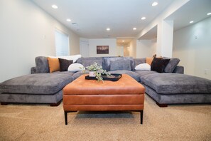 A living room with a sectional sofa, a brown ottoman, and a small table with a plant. - Moody, Modern Comfort in Colorful Colorado! (Loveland)