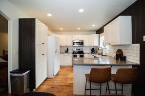 A modern kitchen with white cabinets, a stainless steel refrigerator, a microwave, and a sink. - Moody, Modern Comfort in Colorful Colorado! (Loveland)