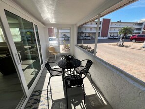 A balcony with a table and chairs, a view of a parking area, and a building in the background. - Casa Blanca - Villa D18 (Sarasota)
