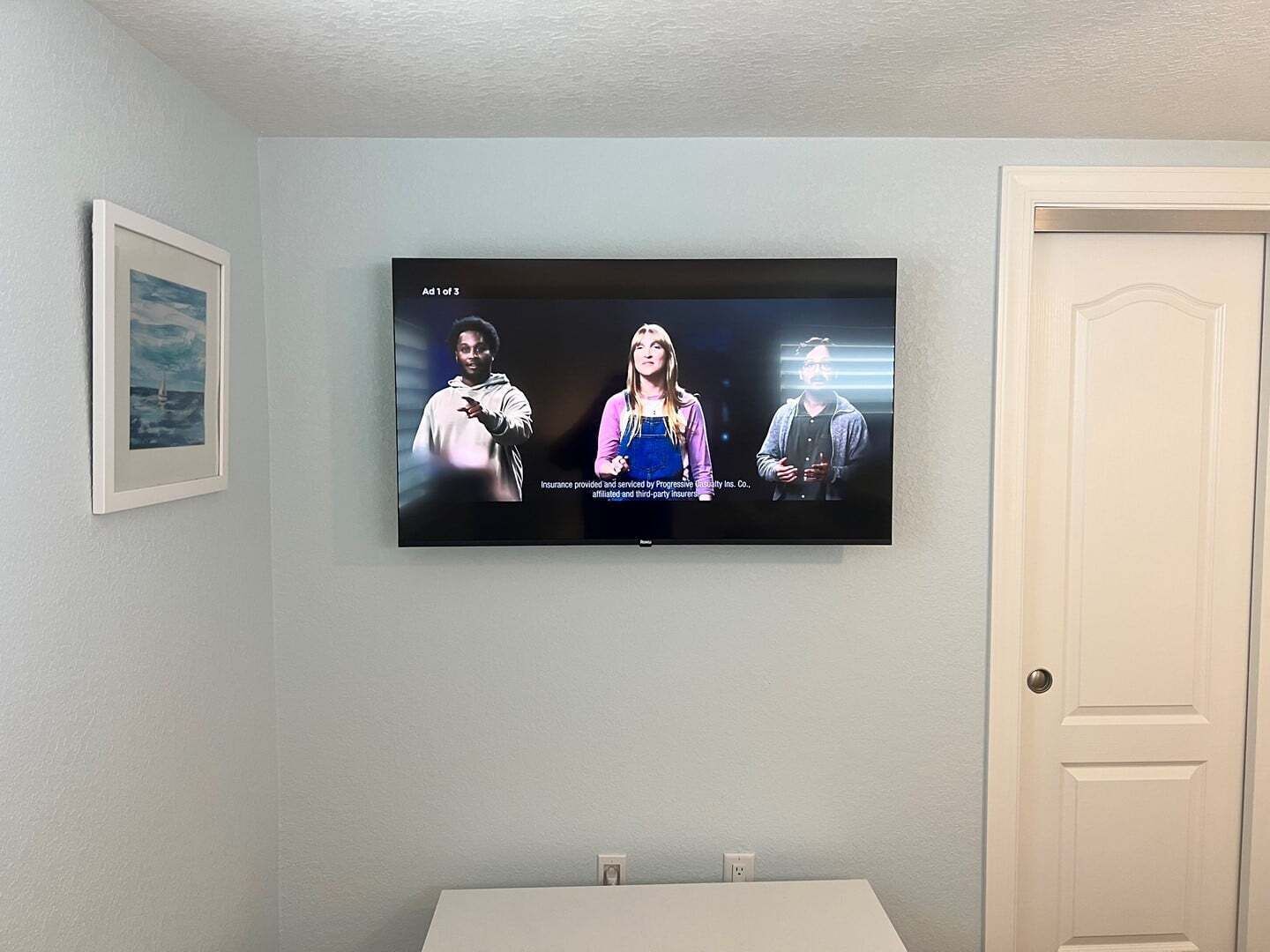 Ein an der Wand befestigter Fernseher mit einem gerahmten Bild daneben.
