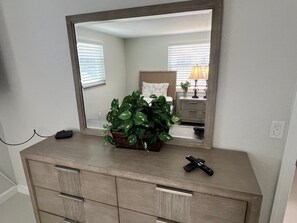 A dresser with a mirror above it, a plant on top, and a remote control on the dresser. - Casa Blanca - Villa D11 (Sarasota)
