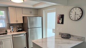 A modern kitchen with stainless steel appliances, a marble countertop, and a wall clock. - Casa Blanca - Villa D11 (Sarasota)