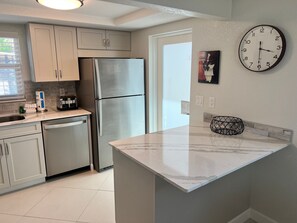 A modern kitchen with stainless steel appliances, a marble countertop, and a wall clock. - Casa Blanca - Villa D11 (Sarasota)