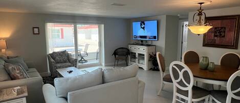 A living room with a sofa, a dining table with chairs, a television, and a ceiling fan.