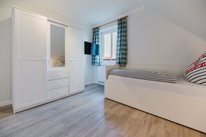 Une chambre avec une armoire blanche, un lit avec une literie à rayures et une fenêtre avec des rideaux à carreaux.