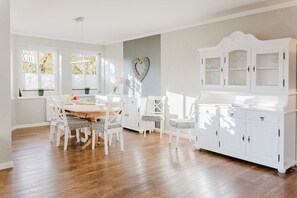 Un coin repas avec une table en bois et des chaises blanches, un meuble blanc aux portes en verre et un élément décoratif mural en forme de cœur.