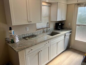 A kitchen with a granite countertop, a sink, a coffee maker, and white cabinets. - Casa Blanca - Villa D05 (Sarasota)