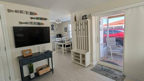 A living room with a flat-screen TV, a dining area with chairs and a table, a white cabinet, and a sliding glass door leading to an outdoor area. - Casa Blanca - Villa D03 (Sarasota)