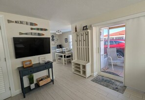 Ein Wohnzimmer mit Flachbildfernseher, einer Essecke mit Stühlen und Tisch, einem weißen Schrank und einer Glastür zum Außenbereich.
