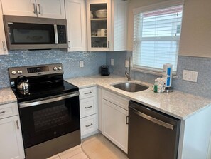 A modern kitchen with stainless steel appliances, white cabinetry, a built-in oven, a microwave, a sink, and a window with blinds. - Casa Blanca - Villa D03 (Sarasota)