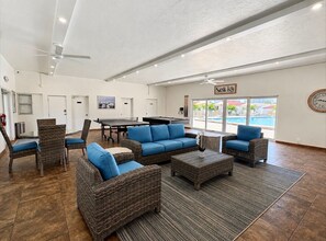 A spacious indoor area with wicker furniture, a pool view, and a clock on the wall. - Casa Blanca  -Villa C15 (Sarasota)