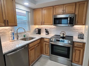 A modern kitchen with wooden cabinets, stainless steel appliances, a built-in microwave, and a kettle on the countertop. - C15 - Your Island Interlude Awaits (Sarasota)