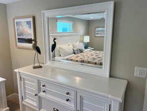 A bedroom with a large mirror, a bed with a floral bedspread, a nightstand with a lamp, and a dresser with drawers. - Casa Blanca  -Villa C15 (Sarasota)