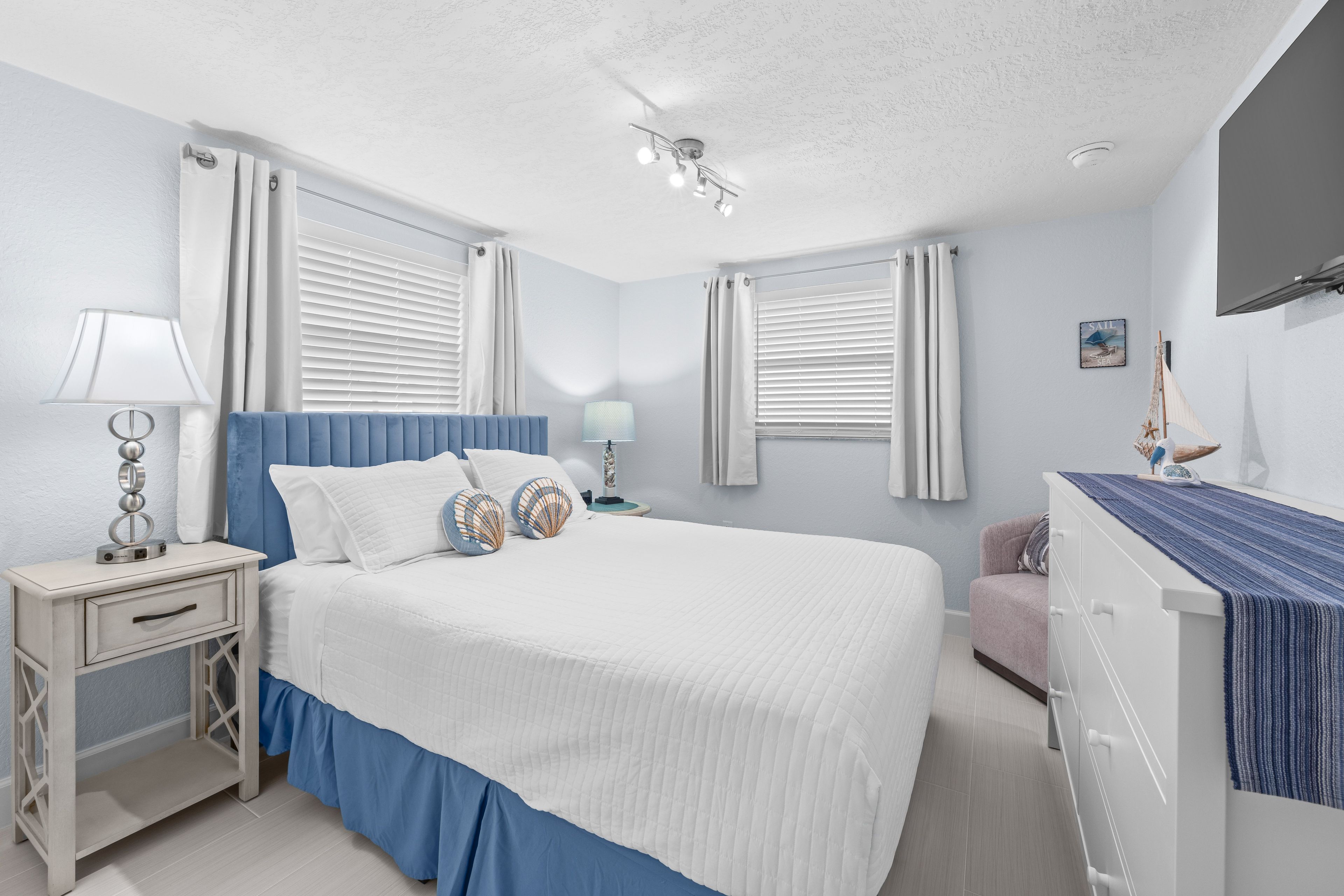 A bedroom with a bed, nightstand, lamp, and a small desk with a chair.