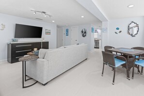 Ein modernes Wohnzimmer mit einer Couch, einem Esstisch mit Stühlen, einem Flachbildfernseher und einer Deckenleuchte.