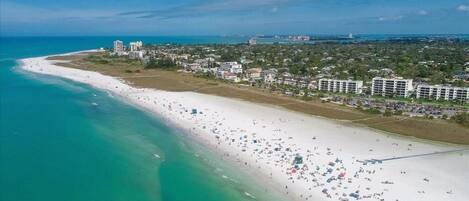 An aerial view of a coastal area with a wide beach, buildings, and a clear sky.