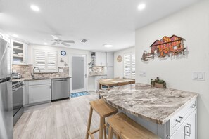 A modern kitchen with white cabinetry, a marble countertop, and a dining area with a wooden table and chairs. - Casa Blanca - Villa C08 (Sarasota)