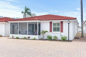 A single-story building with a red-tiled roof, a covered patio area with seating, and a small garden with various plants. - Casa Blanca - Villa C08 (Sarasota)