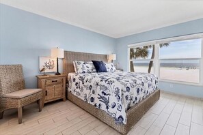 Ein Schlafzimmer mit einem großen Bett, einem Nachttisch, einem Sessel und einem Fenster mit Blick auf den Strand.