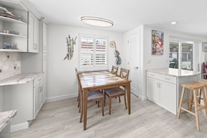 Eine moderne Küche mit weißen Schränken, einem Holztisch und Blick ins Freie.