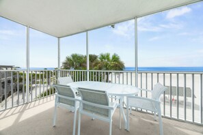 Un balcon avec une table et des chaises blanches, donnant sur une plage et l’océan.