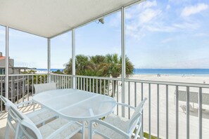 Ein Balkon mit Tisch und Stühlen, der Blick auf einen Strand mit Palmen und einem klaren Himmel gewährt.