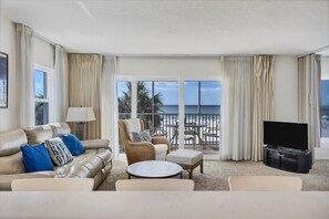 A living room with a sofa, armchair, ottoman, TV, and a view of the beach. - Condo 301 - Standard Plus (Sarasota)