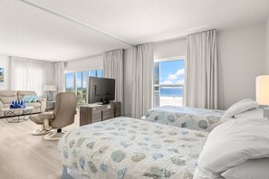 Une chambre d’hôtel avec un lit, un bureau avec une télévision, une chaise et une vue sur la mer.