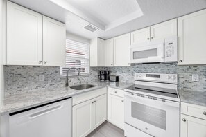 A modern kitchen with white cabinetry, a built-in microwave, a double oven, and a tiled backsplash. - Casa Blanca - Villa C06 (Sarasota)
